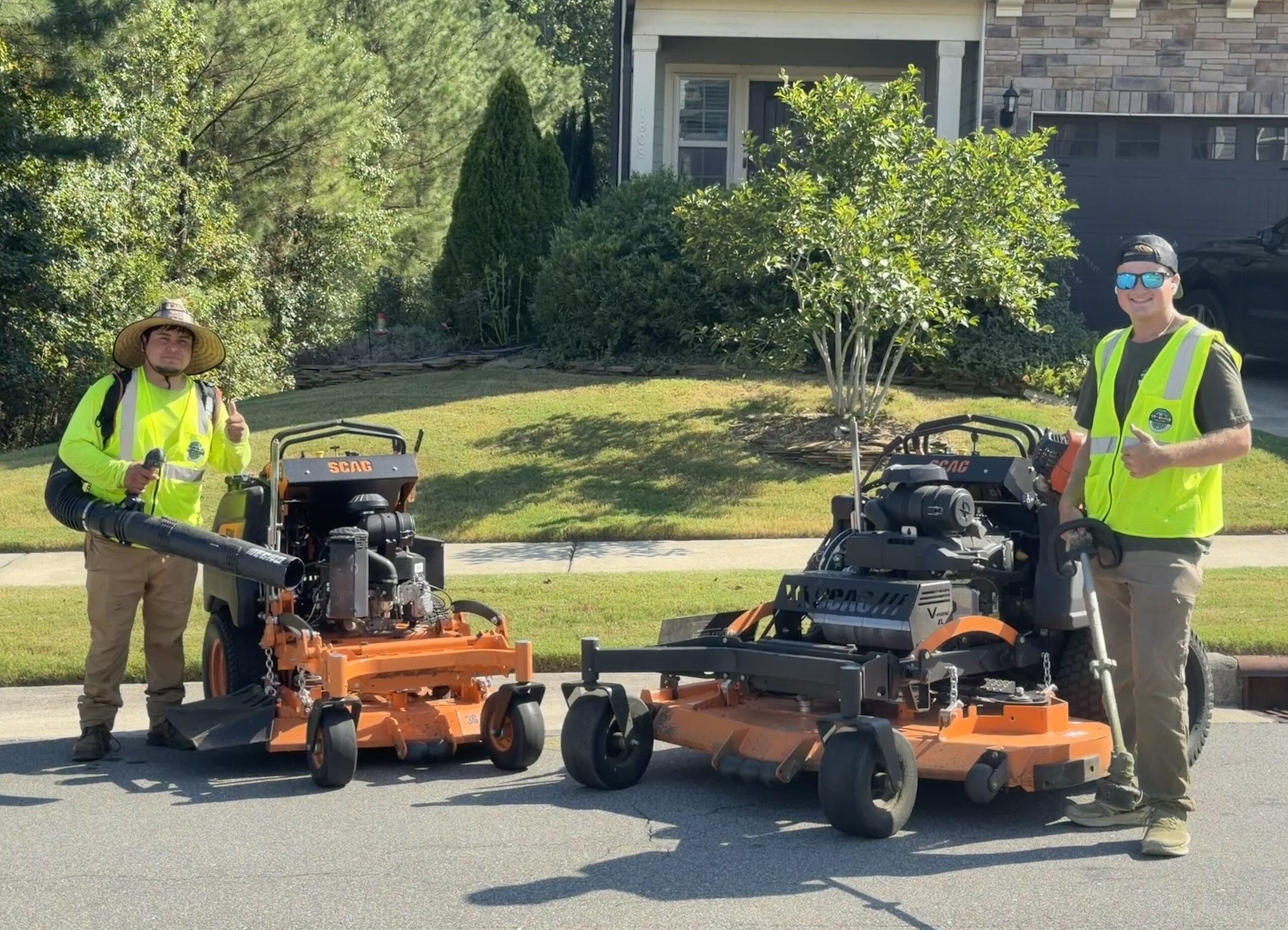 Hector and Mark in front of house showcasing lawn mowing equipment after service